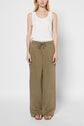 Woman standing against a plain background, wearing a white sleeveless top, loose olive-green drawstring pants, and brown sandals.
