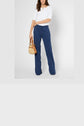 A woman wearing a white short-sleeve top and blue wide-leg pants holds a small woven handbag. Her head is not visible in the image.