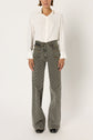 A person wearing a white button-up shirt and gray, taille haute jean flare pants with a subtle motif géométrique, standing against a plain white background.