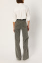 A person stands facing away, wearing a white long-sleeve shirt tucked into high-waisted, wide-leg gray jeans with a motif géométrique. The taille haute style of the jean flare creates a modern silhouette, set against a plain light background.