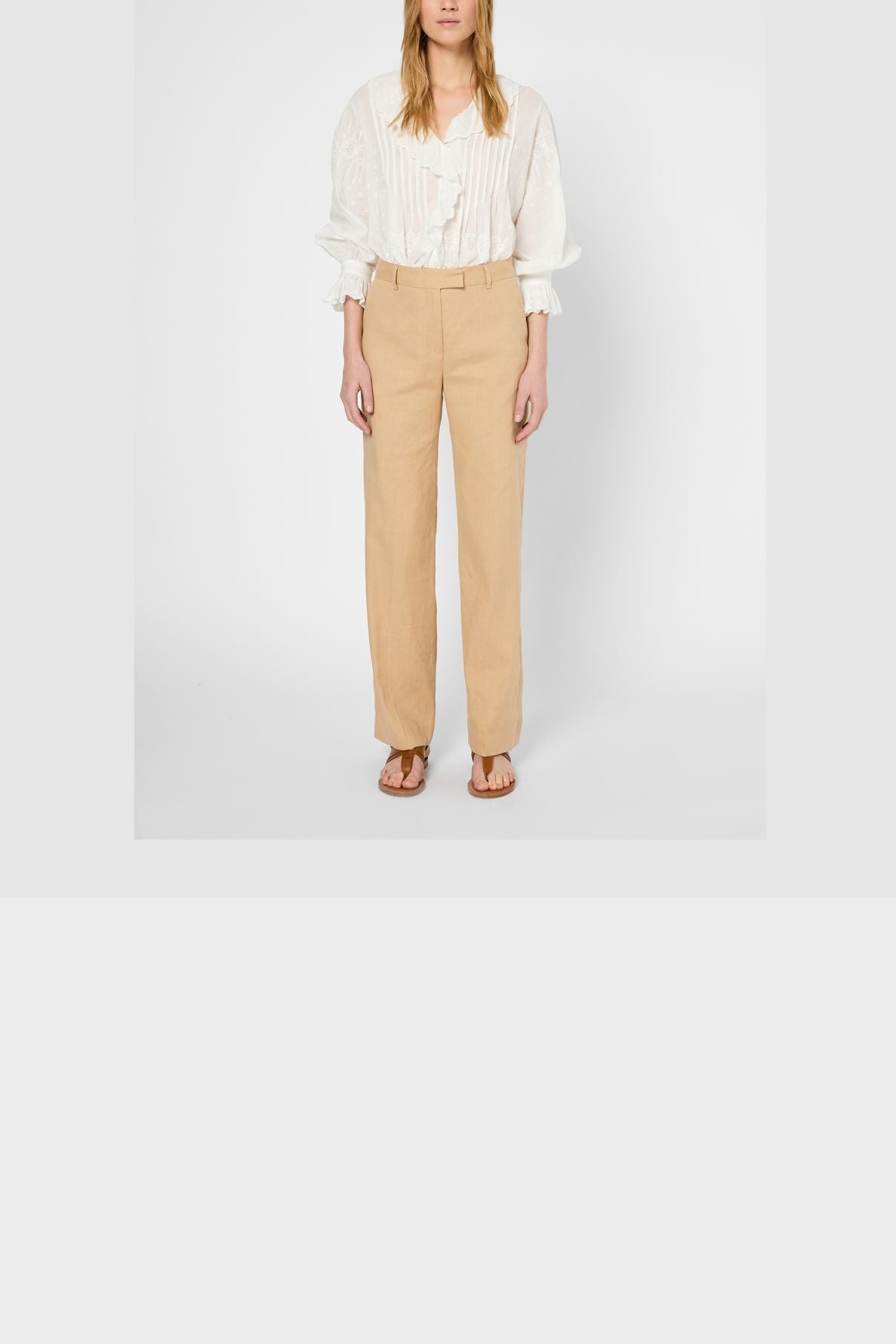 A person wearing a white long-sleeve blouse, a beige pantalon large femme in lin coton, and brown sandals stands against a plain white background.