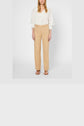 A person wearing a white long-sleeve blouse, a beige pantalon large femme in lin coton, and brown sandals stands against a plain white background.
