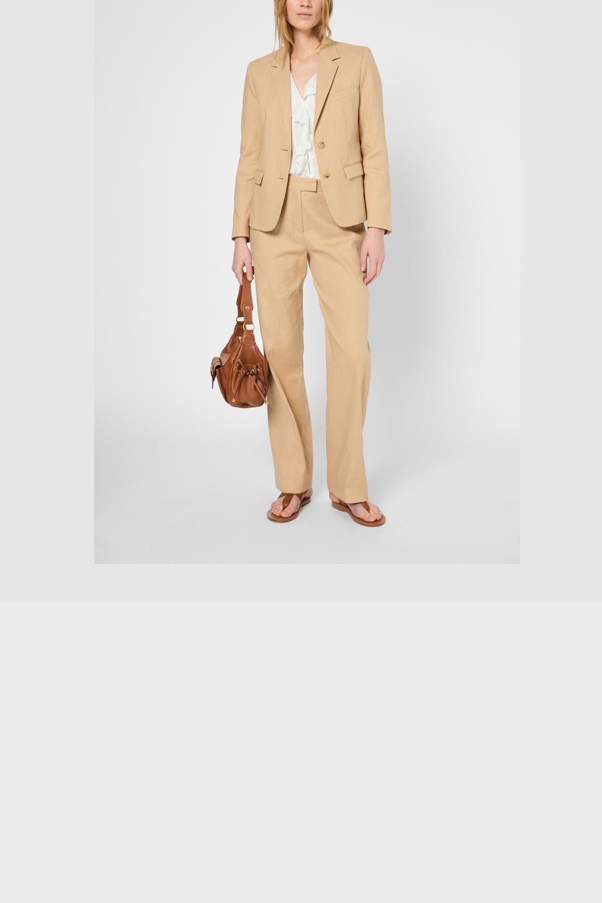 Person wearing a beige suit featuring a pantalon large femme with a white blouse, brown sandals, and holding a brown handbag, standing against a plain white background.