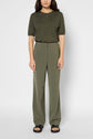 A woman stands against a plain background wearing an olive green short-sleeve top and a pantalon large femme in microfibre kaki, paired with black sandals. Her hair is loose and she has a neutral expression.