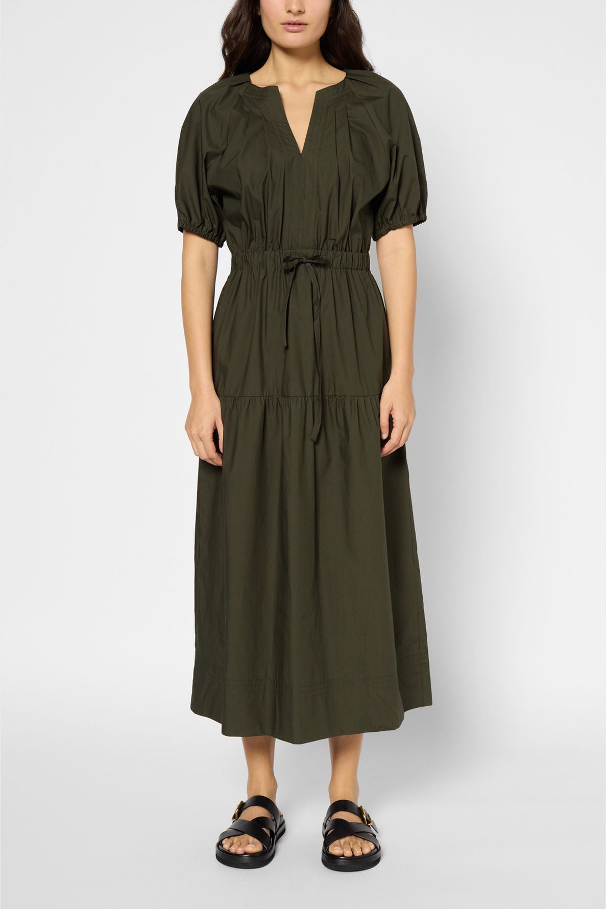 A woman wearing a robe longue in soft popeline kaki, featuring short sleeves, a cinched waist, and black sandals stands against a plain light background.