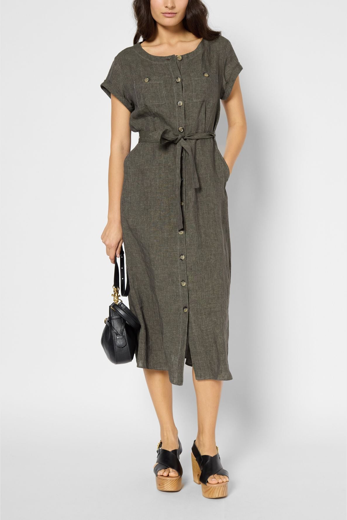 Woman wearing a short-sleeve, button-down, belted midi dress in gray with black platform sandals, holding a small black handbag, standing against a plain background.