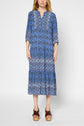 A person wearing a long blue patterned dress with three-quarter sleeves and brown platform sandals, standing against a plain light background.