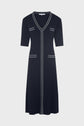 A knee-length navy blue robe cintrée with short sleeves, white vertical piping, a V-neck, and two small front pockets, crafted in comfortable maille stretch fabric and displayed on a plain white background.