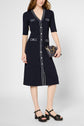 Woman wearing a navy blue, knee-length robe cintrée with white trim, short sleeves, and front buttons. She holds a small black purse with a gold chain and wears black platform sandals.