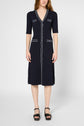 A person wearing a knee-length, short-sleeved, navy blue robe midi with white trim and black platform sandals stands against a plain background.