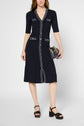 Woman wearing a navy robe midi knee-length dress with white trim, short sleeves, and front buttons. She holds a small black purse with a gold chain and wears black platform sandals.