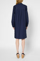 A woman stands facing away, wearing a knee-length, long-sleeve navy blue dress and wooden platform sandals with black straps against a plain background.
