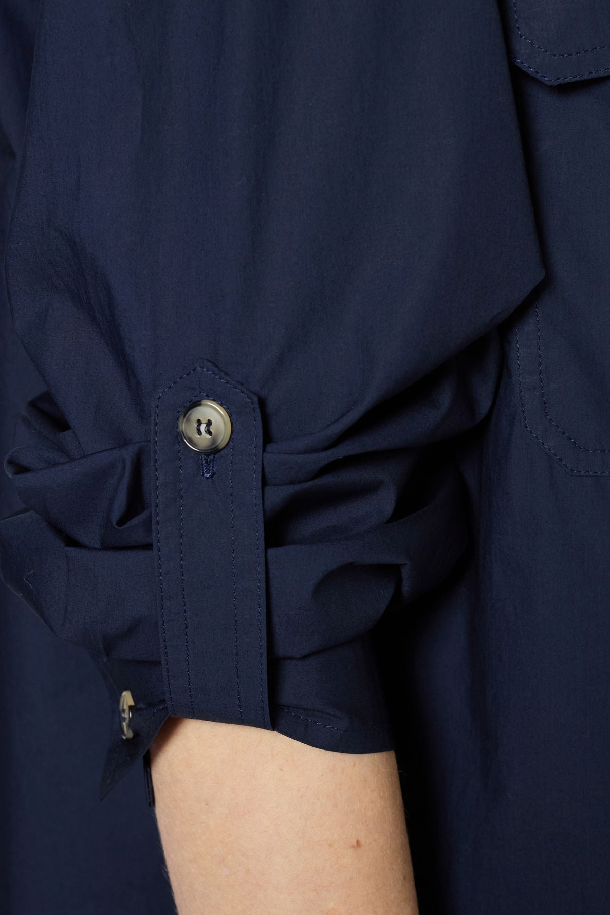 A close-up of a persons arm wearing a dark blue long-sleeve shirt with the sleeve rolled up and buttoned at the cuff. The fabric appears lightweight and slightly wrinkled.