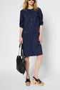 Woman wearing a navy blue button-up dress with front pockets, black platform sandals, and holding a black handbag with a chain strap. She has wavy blonde hair and is standing against a plain background.