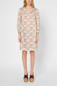A person stands wearing a knee-length dress with a colorful geometric pattern, long sleeves, and brown platform sandals. The background is plain white.