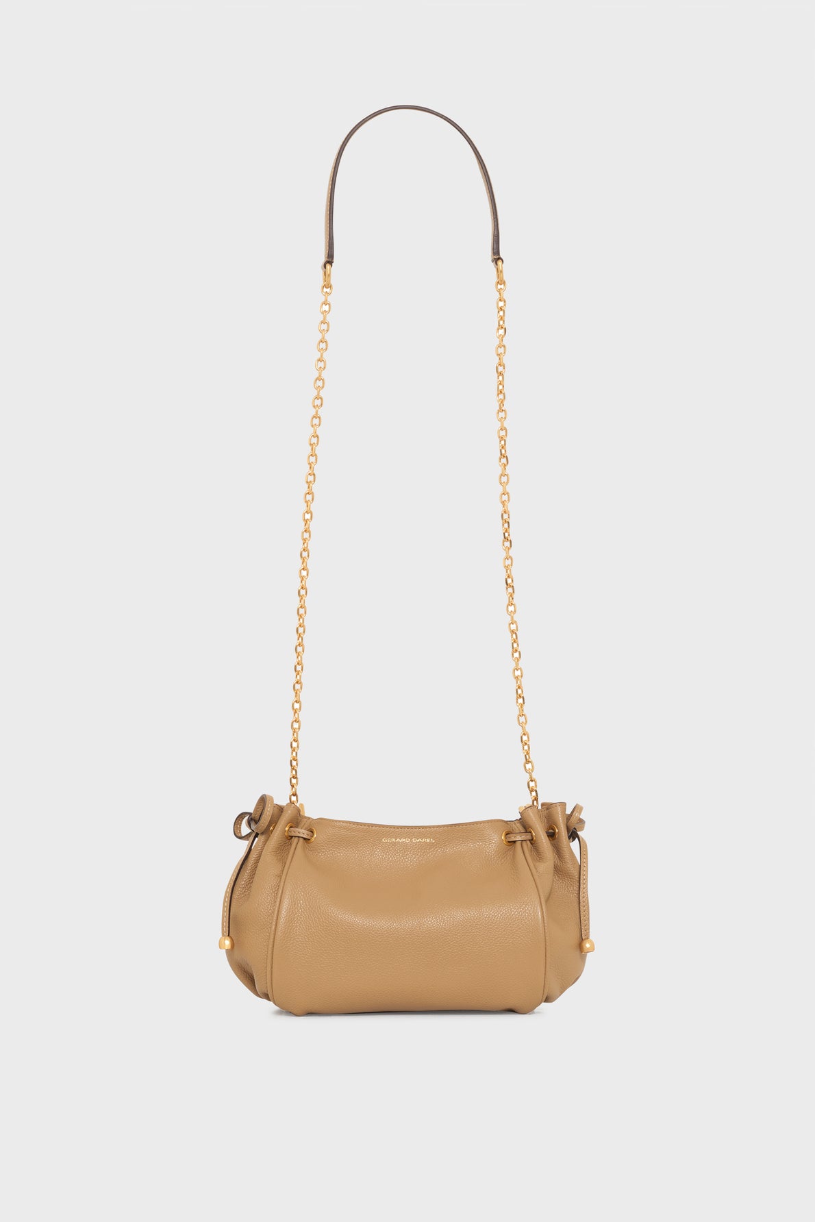 Tan Gerard Darel sac bandoulière crafted from cuir grainé leather, featuring a rounded shape, gold chain strap, and drawstring closures on both sides, set against a plain white background.