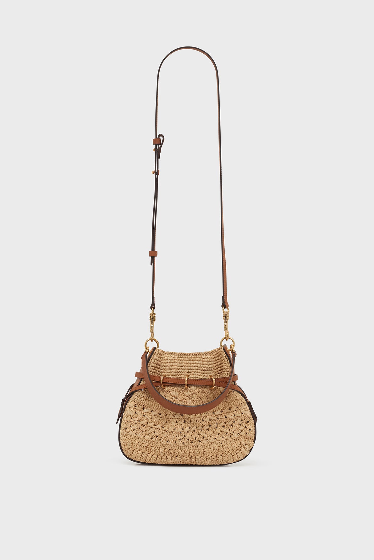 Woven straw shoulder bag with brown leather trim and handle, gold hardware, and an adjustable leather strap, showcased against a plain white background—a sac seau mini that effortlessly blends cuir et raphia, highlighting exceptional savoir-faire artisanal.