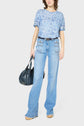 A person wearing a light blue paisley shirt and high-waisted wide-leg jeans holds a dark handbag. The outfit includes a black belt and beige shoes. The background is plain white.