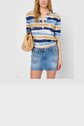 Woman wearing a blue, brown, and white striped top with a short denim skirt, holding a small woven straw purse. Her hair is loose, and the background is plain white.
