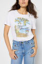 A woman wears a white French Riviera t-shirt with a lemon tree and balcony graphic, paired with high-waisted blue jeans.