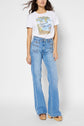 Woman wearing a white printed t-shirt with blue high-waisted flared jeans and tan platform shoes, standing against a plain light background.