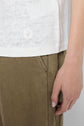 A person wearing a white débardeur lin and olive green pants stands with their right arm relaxed by their side, only the torso and hand are visible.