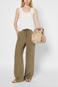 A woman wearing a white débardeur été, olive wide-leg pants, and sandals holds a beige handbag. She stands against a white background.