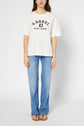 A person stands facing forward, wearing a T-shirt blanc en coton G. Darel Saint-Tropez à manches courtes, paired with light blue jeans and brown sandals, against a plain light background.