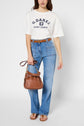 Woman wearing a white G.DARE Saint-Tropez T-shirt blanc en coton à manches courtes, light blue jeans, brown belt, tan sandals, and holding a brown handbag against a plain background.