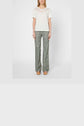 A woman stands facing forward, wearing a white T-shirt lin à manches courtes with delicate col rond brodé and lace detail, paired with patterned flare pants and tan platform shoes against a plain light background.