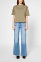 A person wearing a loose olive green t-shirt and light blue wide-leg jeans with front slits, standing against a plain white background.