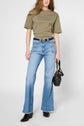 A person wearing a khaki t-shirt, light blue flared jeans with front pockets, black belt, black heeled boots, and holding a small black handbag, standing against a plain background.