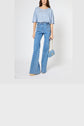 Woman wearing a t-shirt ample casual in light blue, paired with high-waisted blue patterned flare jeans and holding a small blue handbag with a gold chain, standing against a plain white background.