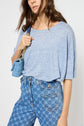 A woman wears a t-shirt ample casual in light blue, tucked into high-waisted patterned blue jeans and carries a small blue purse on her shoulder.