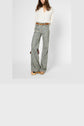 Woman wearing a white blouse with manches 3/4, a brown belt, and high-waisted wide-leg floral pants with platform shoes, standing against a plain light background. Her face is partially out of frame.