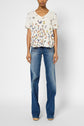 A person wearing a white col V T-shirt oversize with colorful imprimé papillons and blue flared jeans stands against a plain background.