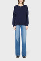 A person stands facing forward, wearing a loose navy blue sweater and light blue flared jeans with black shoes, against a plain white background.