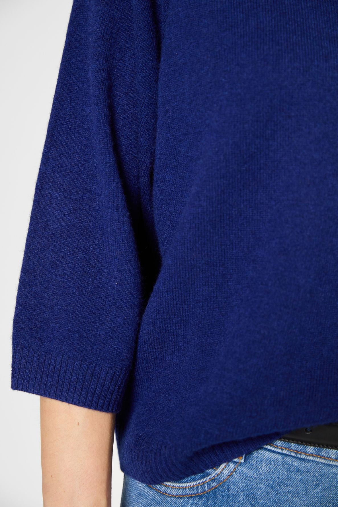 A close-up of a persons torso wearing a dark blue knit sweater with three-quarter sleeves and blue jeans.