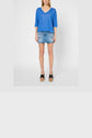 Woman wearing a blue V-neck top, denim mini skirt, and black open-toe wedge sandals, standing against a plain white background.