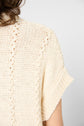 A close-up of a person wearing a light beige, textured knit short-sleeve sweater. Only part of the back and shoulder are visible. The knit features vertical patterns and rolled sleeve cuffs.