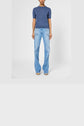 Person wearing a blue short-sleeve top and light blue flared jeans with large front pockets, standing against a plain white background.