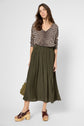 Woman wearing a pull léopard à col V, olive green pleated skirt, and brown platform sandals stands against a plain background, holding a textured handbag by her side.
