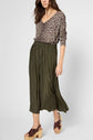 A person wearing a pull léopard à col V, an olive green pleated midi skirt in lin coton, and brown platform sandals. The image is shot from the knees up with a neutral background.