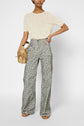 Woman wearing a sheer cream t-shirt reminiscent of a pull manches courtes, high-waisted floral wide-leg pants, sandals, and holding a tan handbag stands against a plain background.