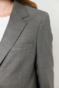 Close-up of a person wearing a gray blazer femme over a white top. Only part of the person’s chest, shoulder, and hair are visible, with a focus on the veste tailleur’s lapel and pocket.