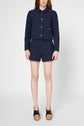 A person wearing a navy blue jacket with buttons and matching high-waisted shorts, standing against a plain white background, with black platform sandals.