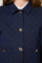 A close-up of a person wearing a navy blue patterned jacket with shiny gold buttons over a white shirt. The jacket has a collar and two front pockets.