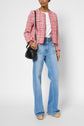 Person wearing a veste courte femme in red tweed, a white top, light blue wide-leg jeans, tan shoes, and carrying a small black shoulder bag stands against a plain background.