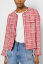 A woman wearing a veste courte femme—specifically, a red and white tweed jacket with frayed edges—paired with a white top and blue jeans with patch pockets, shown from shoulders to hips.