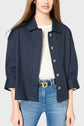 Woman wearing a navy veste oversize button-up jacket over a white knit top and blue jeans, with a black belt. Her hair is down and her face is partially out of frame.